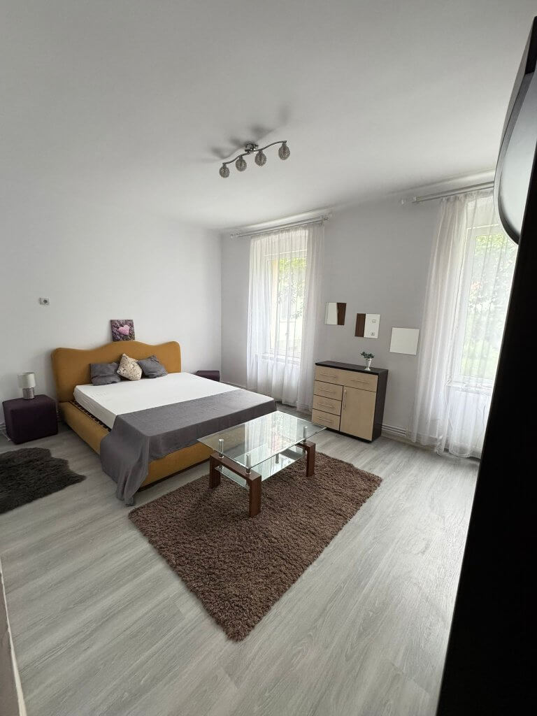 Dormitor luminos cu pat dublu și masă de sticlă.